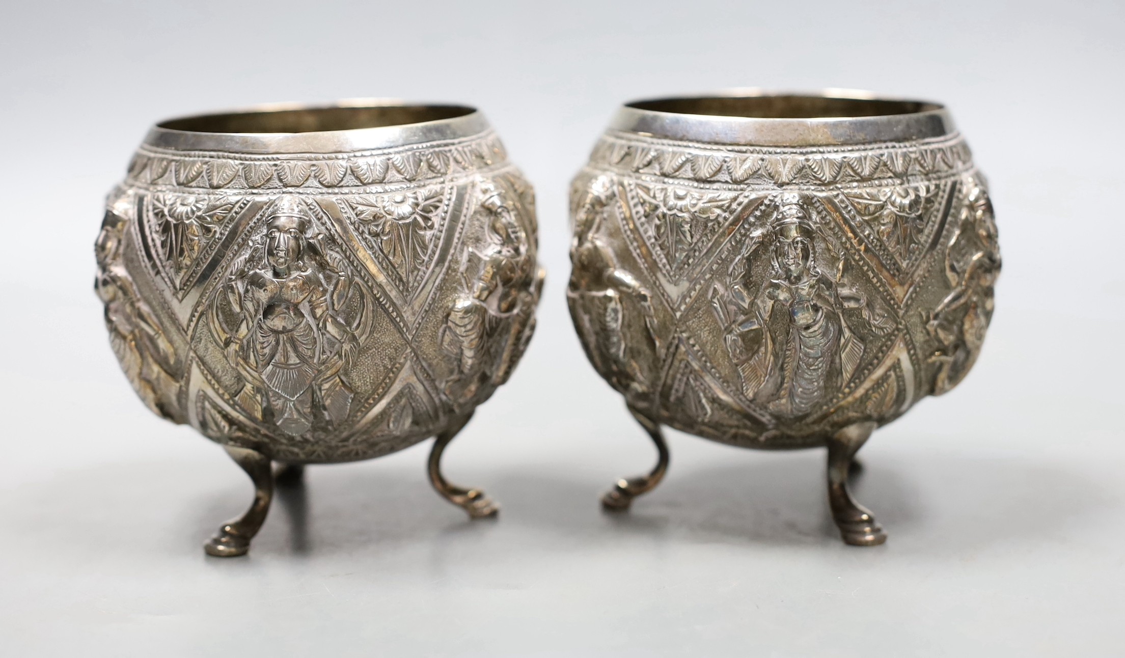 A pair of Indian embossed white metal circular bowls, on three hoof feet, height 82mm.
